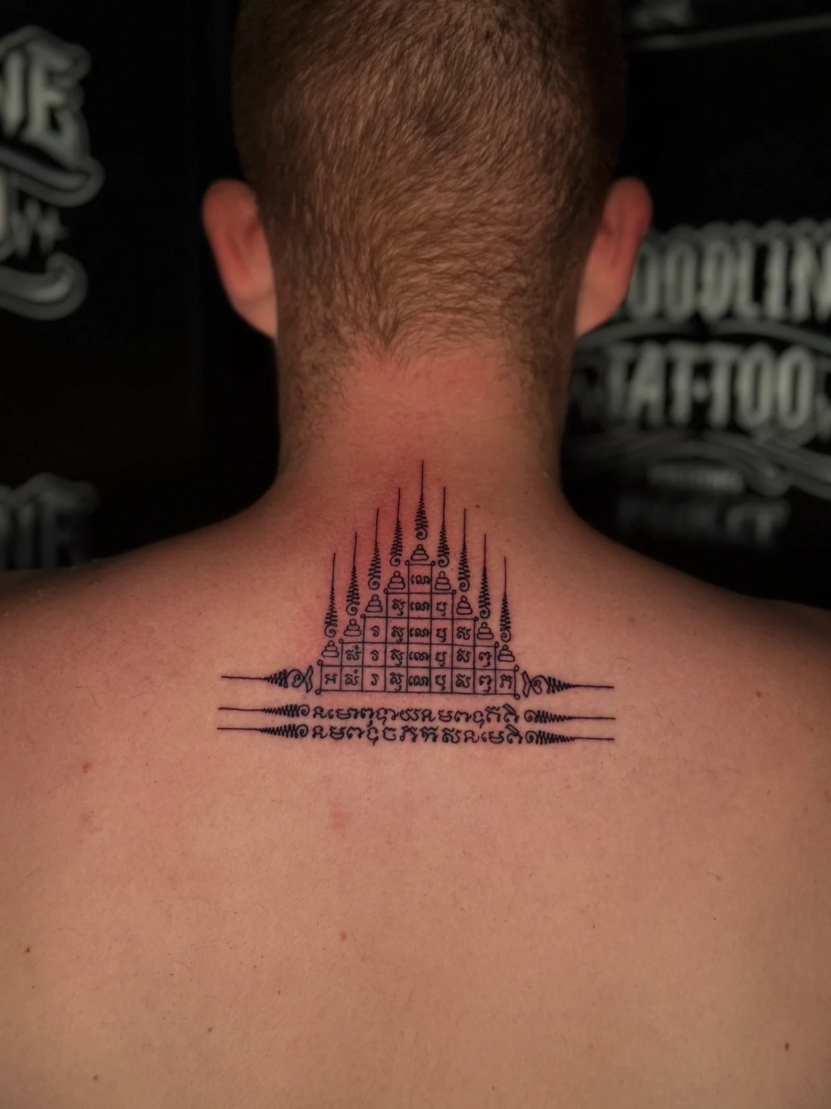 Gao Yord (Nine Spires) Sak Yant with a geometric pyramid grid of Khom script and nine peaked unalomes centered on the upper back at Bloodline Tattoo Phuket.