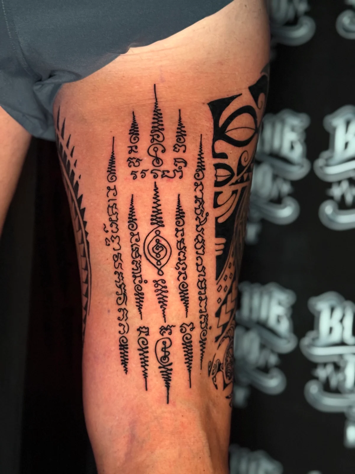 Hah Taew (Five Lines) Sak Yant with five vertical Khom script rows, unalomes, and a central diamond eye motif on the upper thigh at Bloodline Tattoo Phuket.