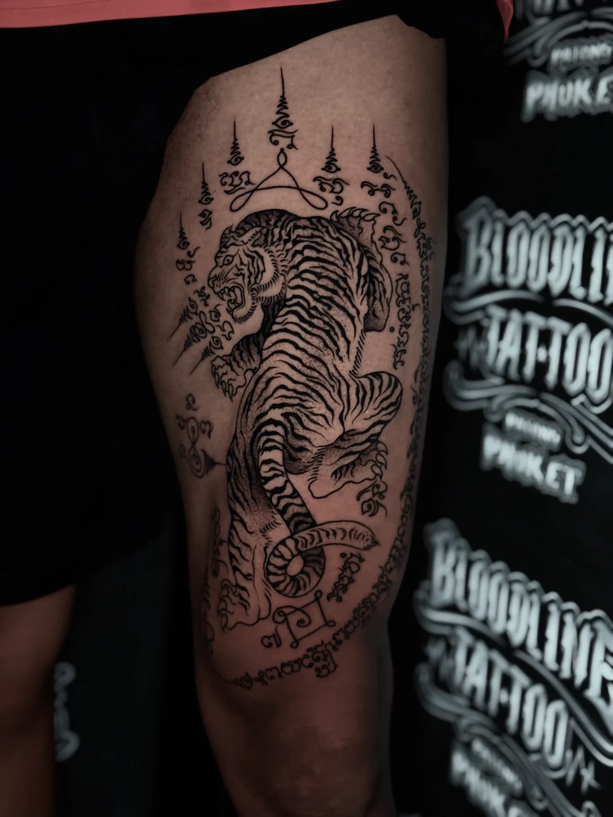 Suea (Tiger) Sak Yant of a snarling tiger with Khom script border and multiple unalomes on the outer thigh at Bloodline Tattoo Phuket.