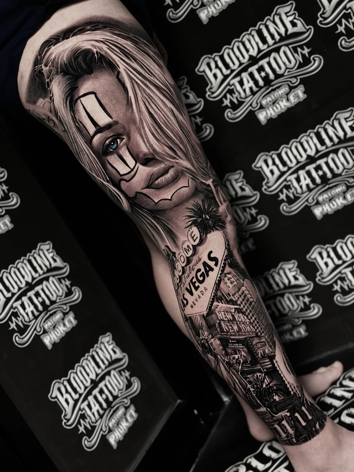 Chicano payasa portrait leg sleeve with blue eye and Las Vegas cityscape at Bloodline Tattoo Phuket.