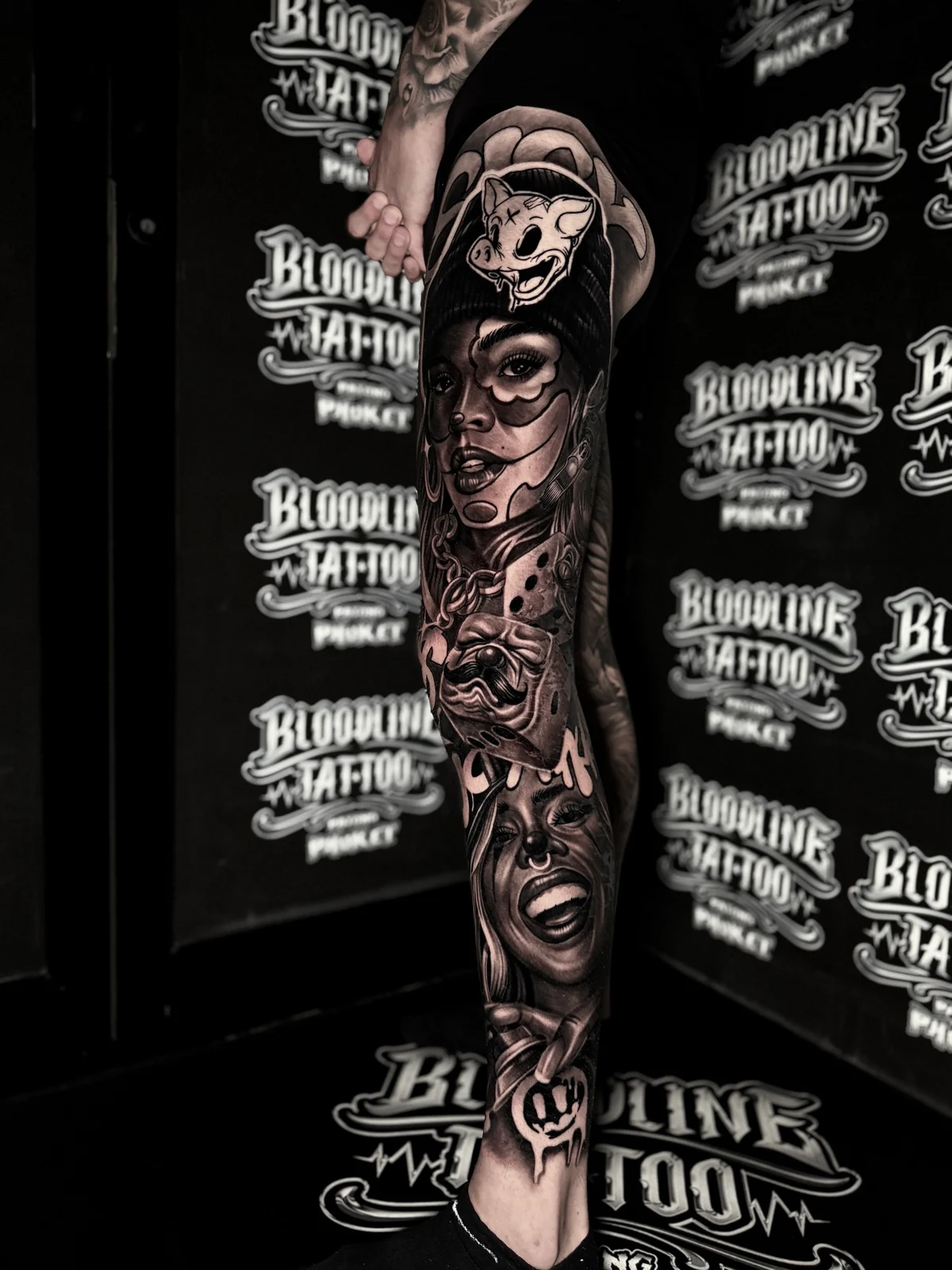 Chicano payasa and laughing portrait leg sleeve with dice, chain, and graffiti logo at Bloodline Tattoo Phuket.