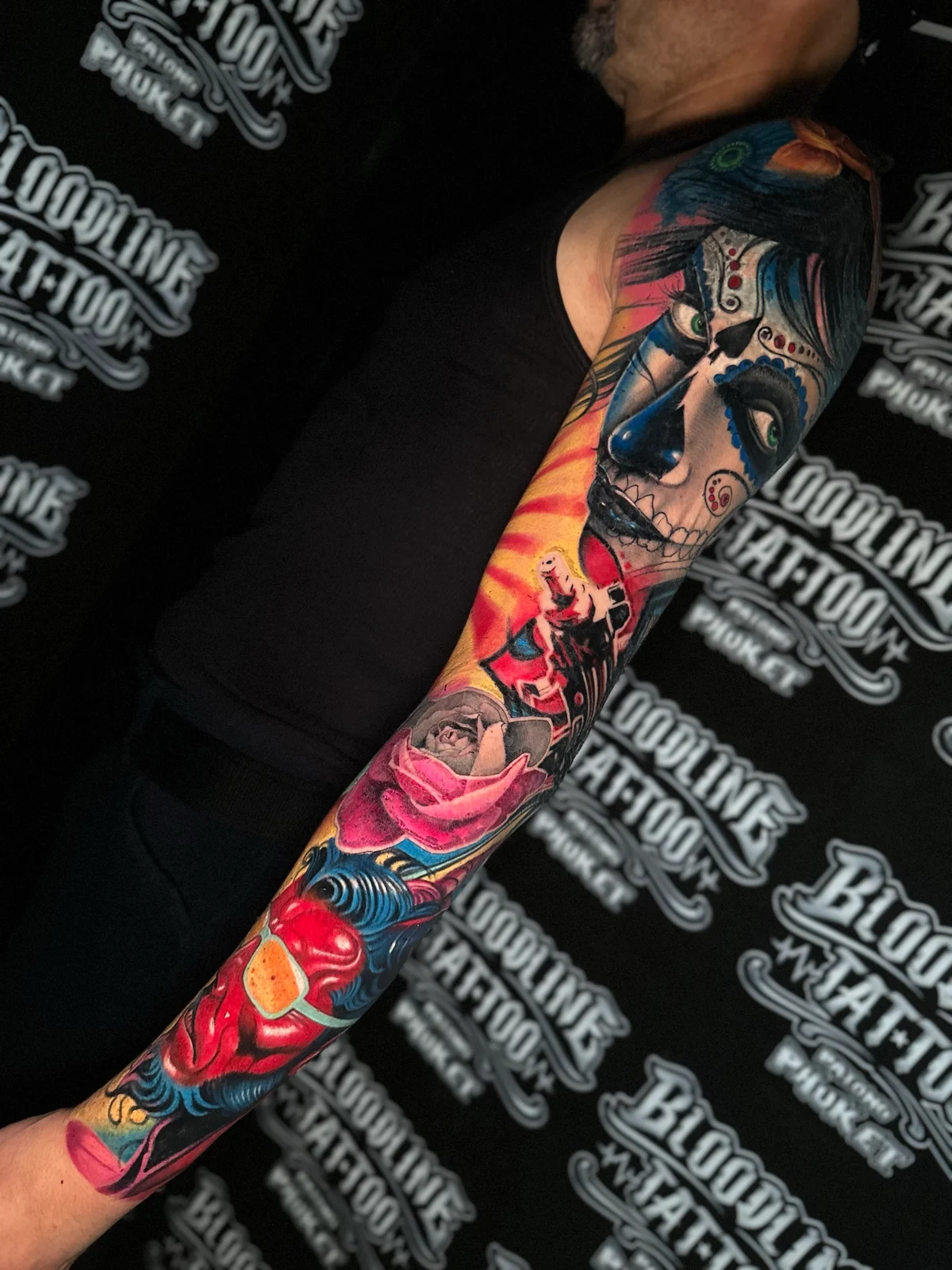 Colour sleeve with a Santa Muerte portrait, a pink rose, and a red demonic face on yellow and blue ornamental backgrounds at Bloodline Tattoo Phuket.