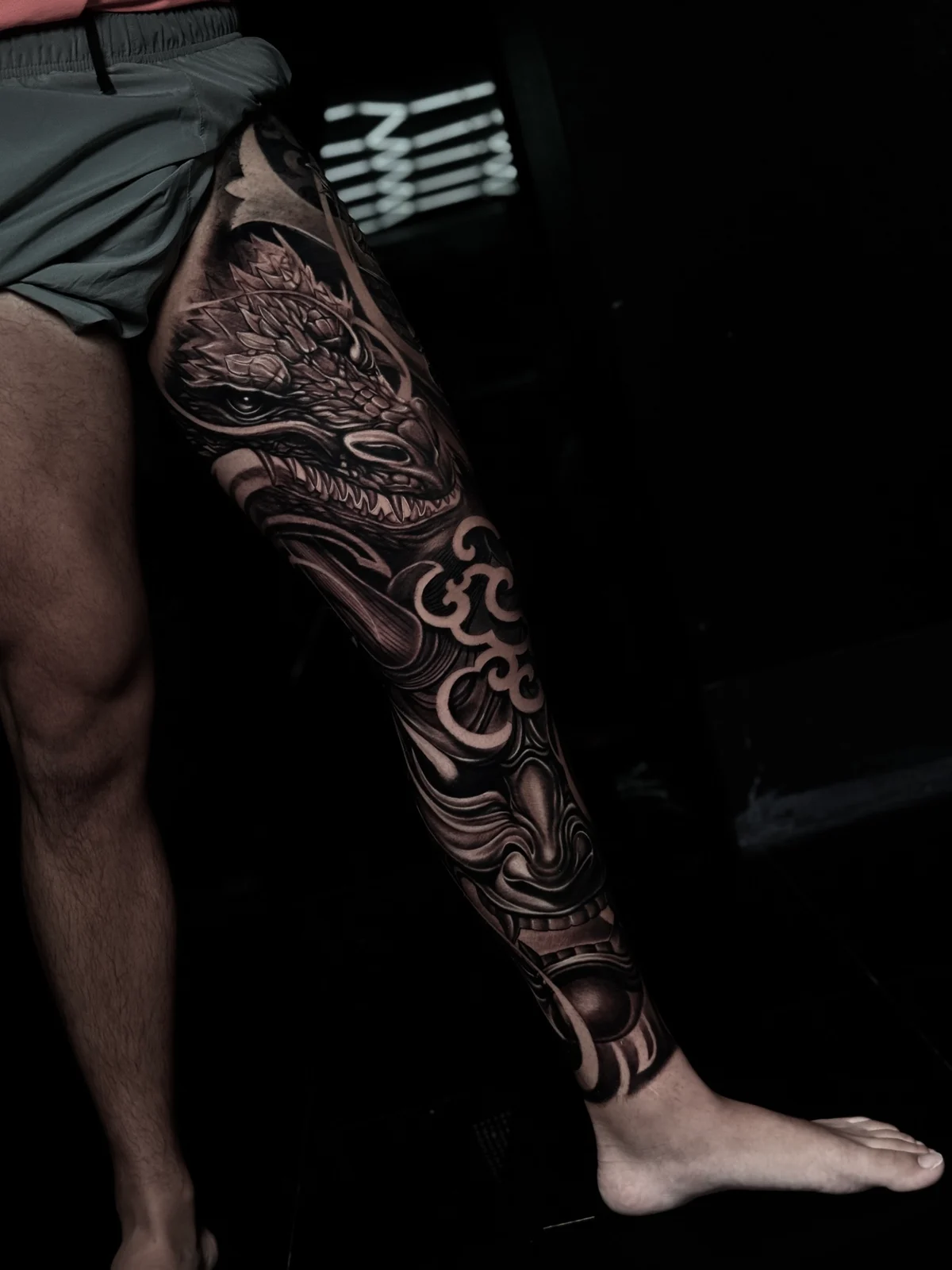 Japanese black and grey full leg sleeve with a dragon on the thigh and Hannya mask on the shin amid clouds and waves at Bloodline Tattoo Phuket.