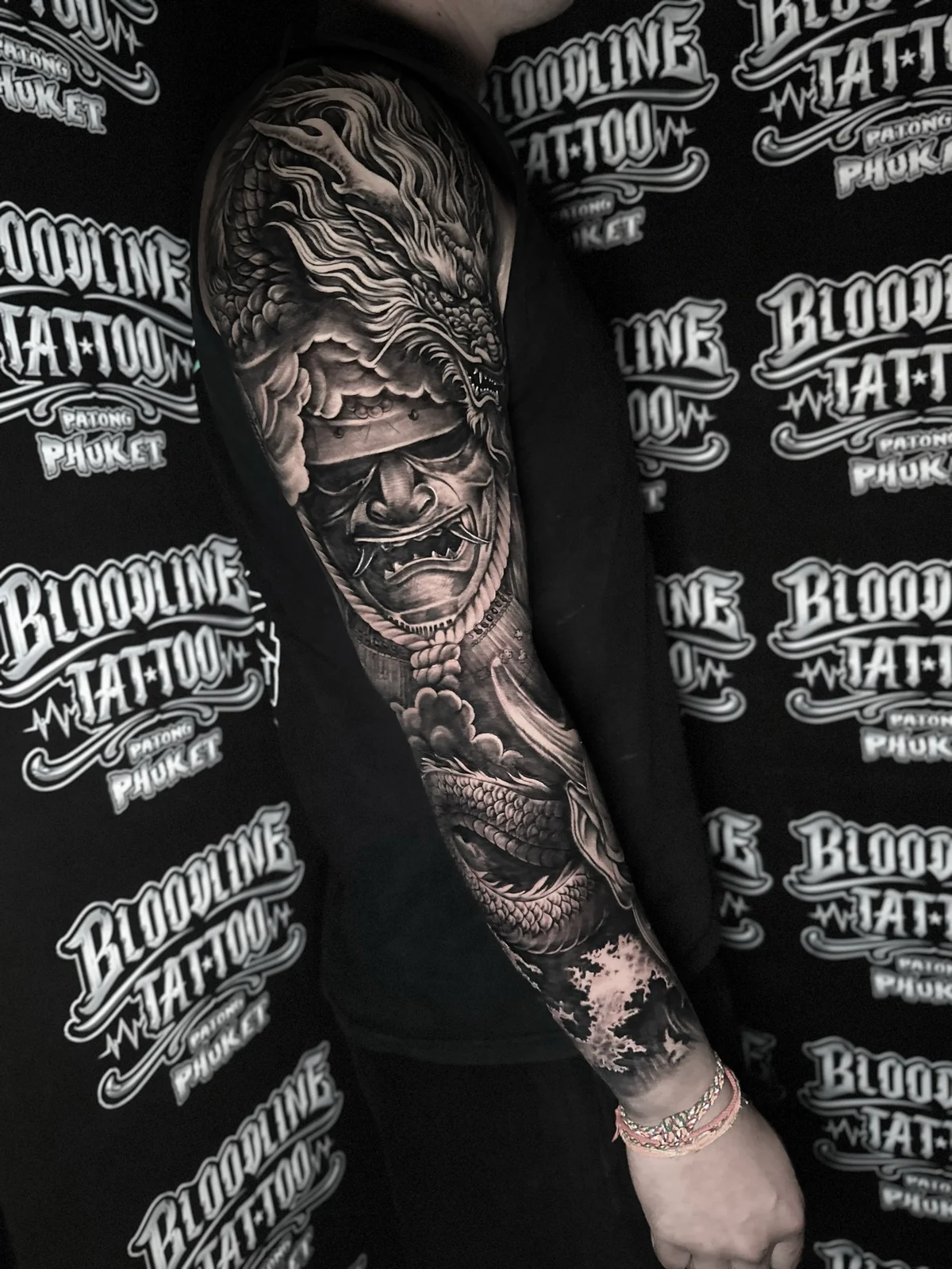 Japanese black and grey full sleeve with dragon head and menpo on the upper arm, scaled body on the forearm, and crashing waves at the wrist at Bloodline Tattoo Phuket.