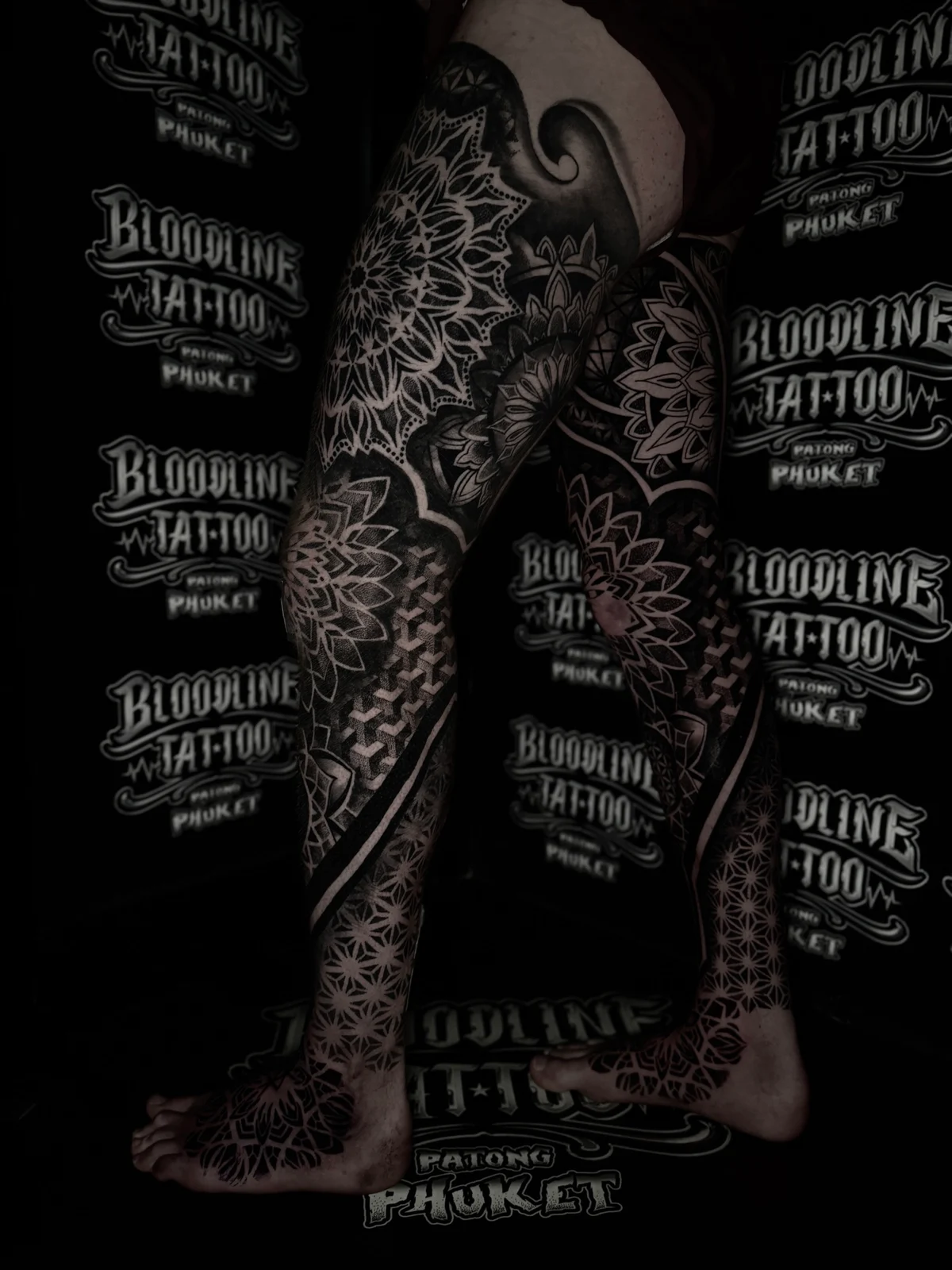 Front-facing dual full leg sleeves with thigh and knee mandalas, stacked 3D cube geometry on the shins, and fine dotwork covering the feet, at Bloodline Tattoo Phuket.