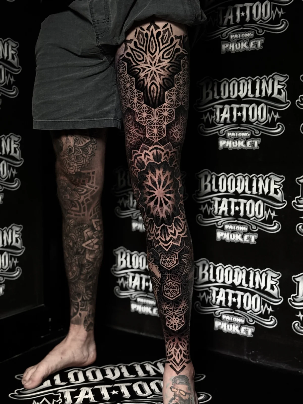Front-facing full leg mandala sleeve with honeycomb thigh geometry, a bold knee lotus mandala, and flowing dotwork panels down to the ankle, inked at Bloodline Tattoo Phuket.