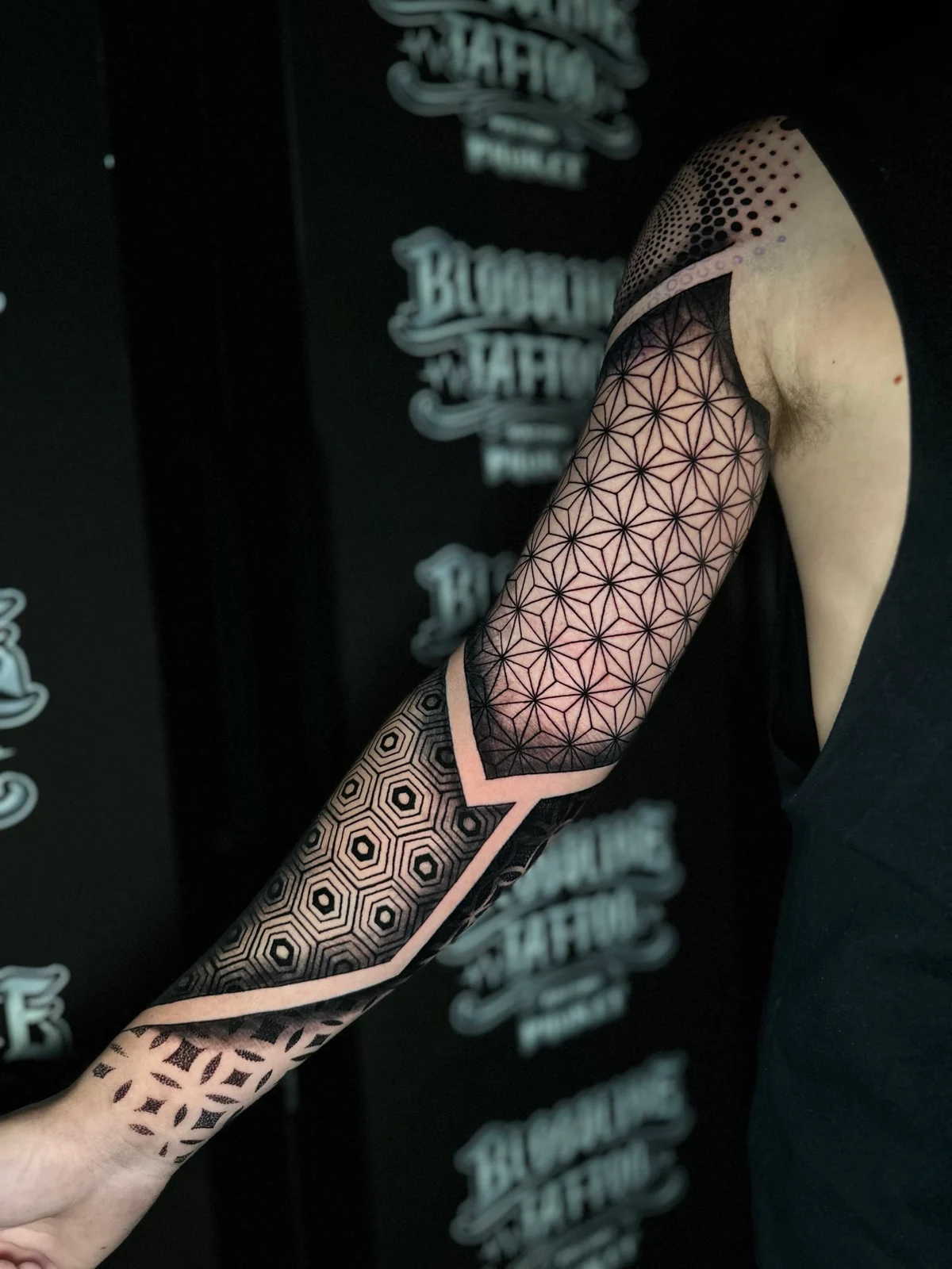 Geometric mandala sleeve with Asanoha triangle upper arm panels, a bold elbow band, and concentric 3D-shaded hexagons on the forearm at Bloodline Tattoo Phuket.