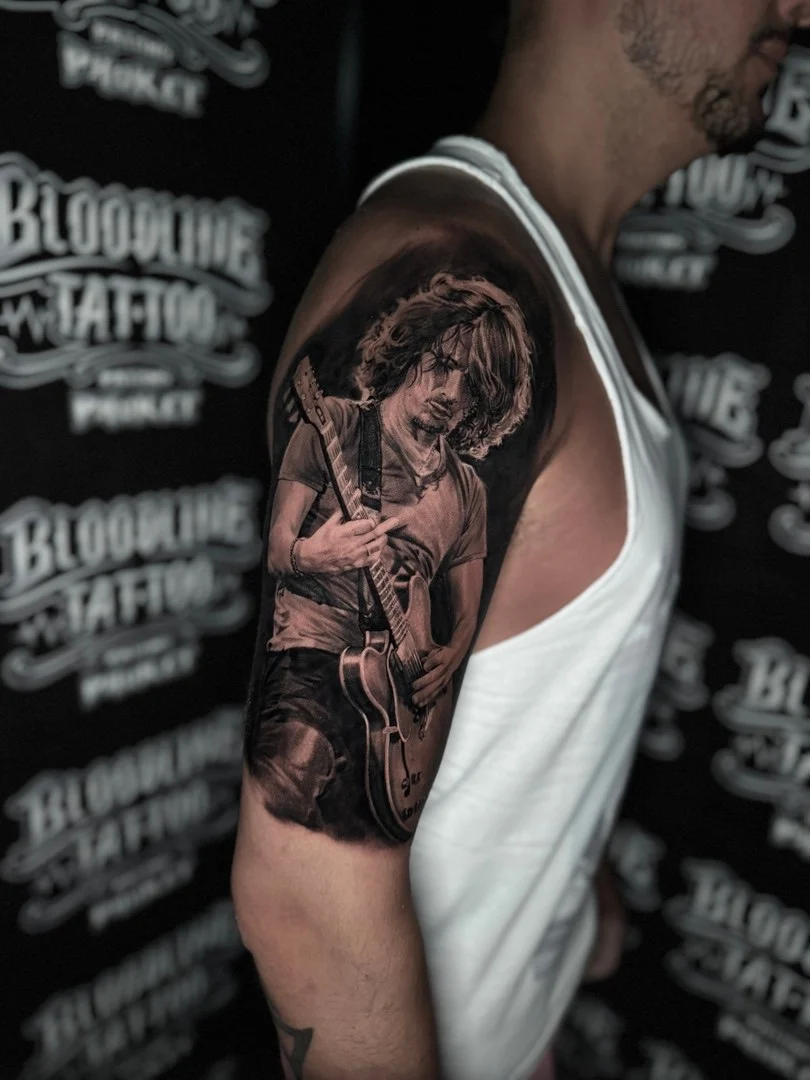Black and grey portrait realism shoulder tattoo of Chris Cornell playing electric guitar at Bloodline Tattoo Phuket.