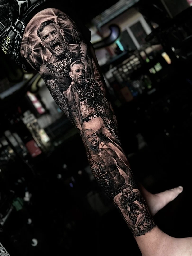 Black and grey portrait realism UFC leg sleeve with Conor McGregor and Jon Jones championship scenes at Bloodline Tattoo Phuket.