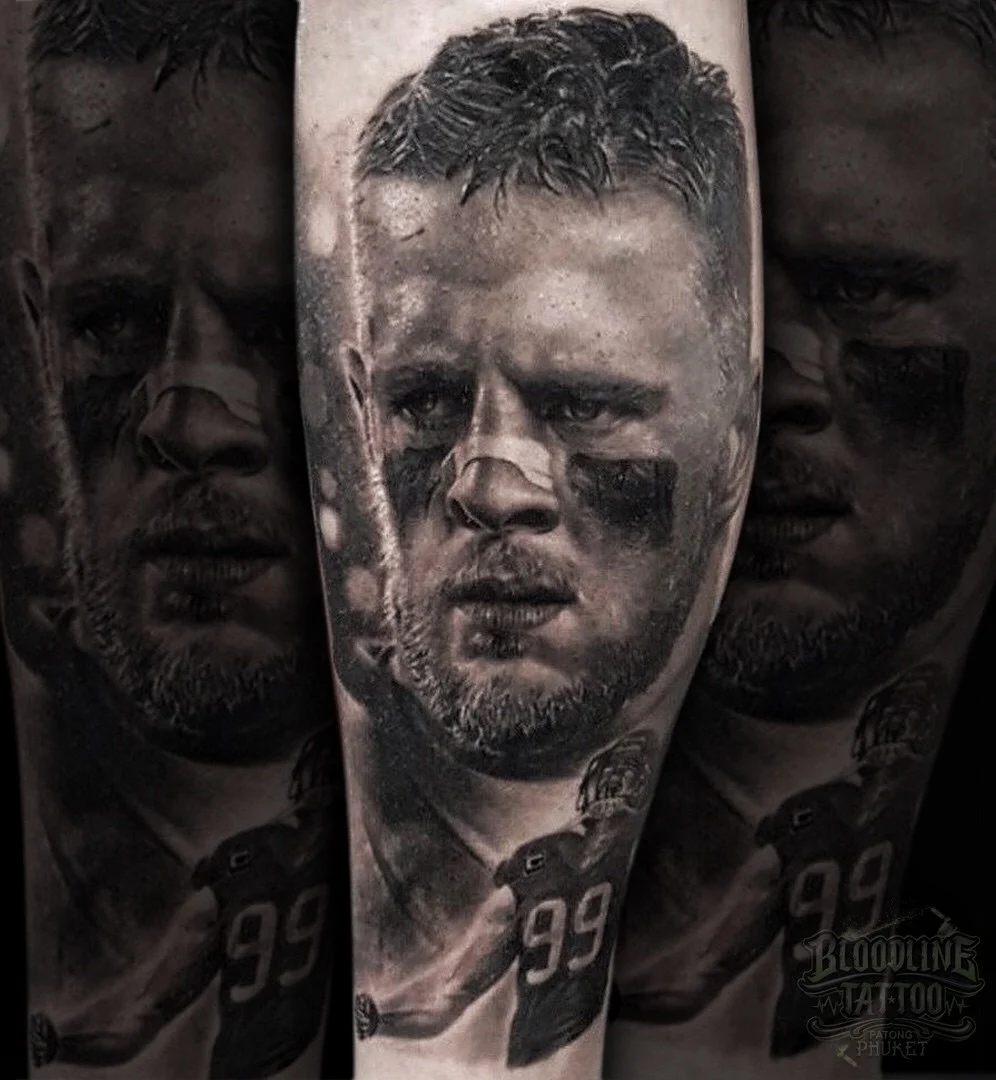 Black and grey portrait realism leg tattoo of J.J. Watt with eye black, nose tape, and number 99 football figure at Bloodline Tattoo Phuket.