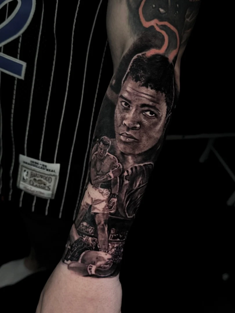 Black and grey portrait realism forearm tattoo of Muhammad Ali above the Sonny Liston knockdown boxing scene at Bloodline Tattoo Phuket.