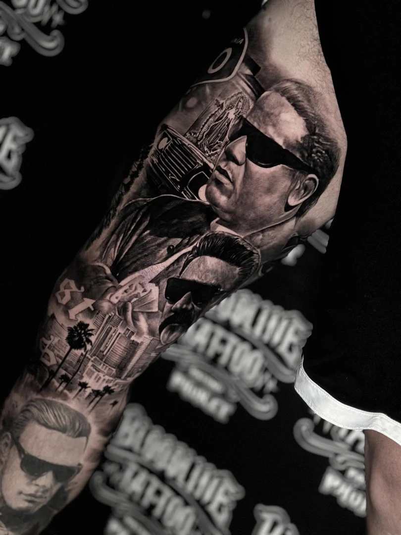 Black and grey portrait realism arm sleeve with sunglasses portraits, playing cards, and cityscape filigree at Bloodline Tattoo Phuket.