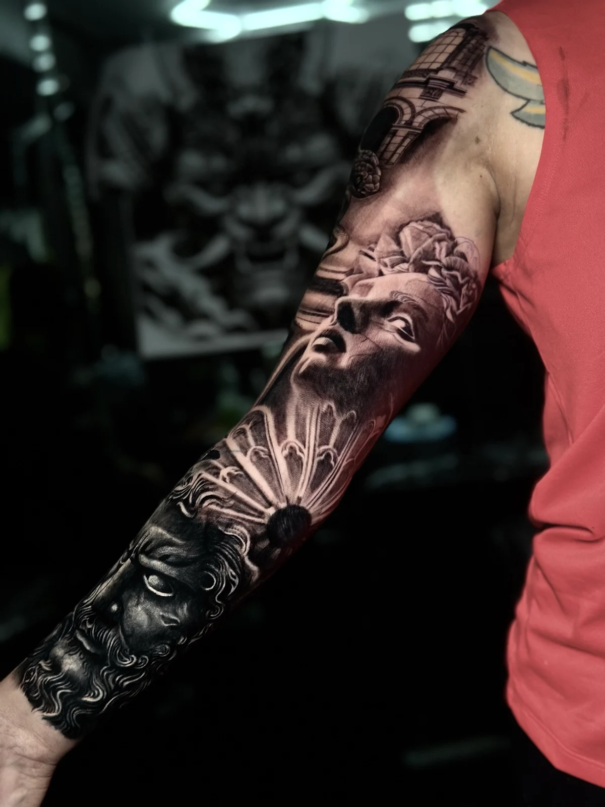 Detailed black and grey realism full sleeve tattoo featuring classical statue faces and architectural elements at Bloodline Tattoo Phuket.