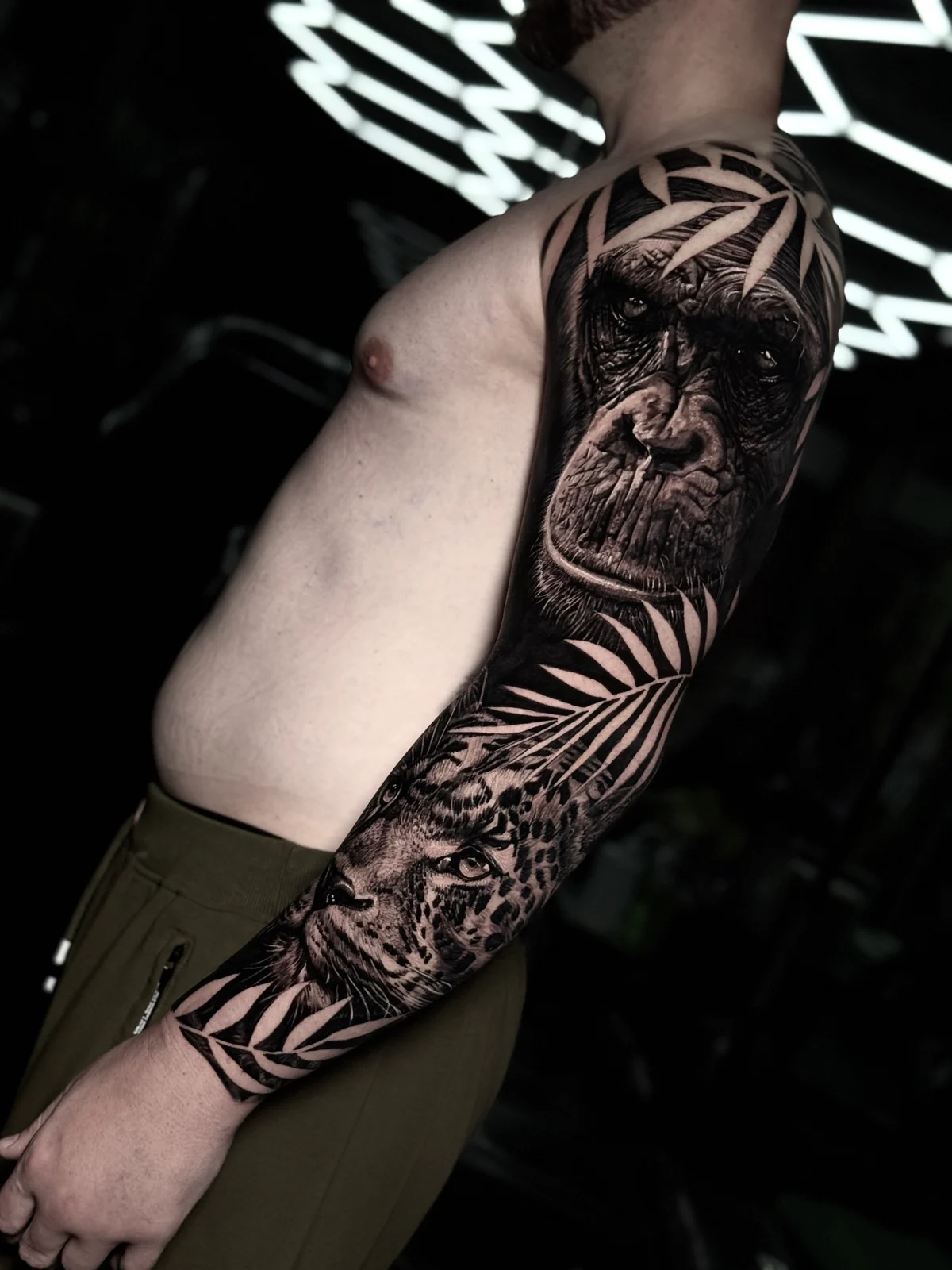Detailed black and grey realism full sleeve tattoo featuring realistic chimpanzee and leopard portraits framed by tropical palm fronds at Bloodline Tattoo Phuket.